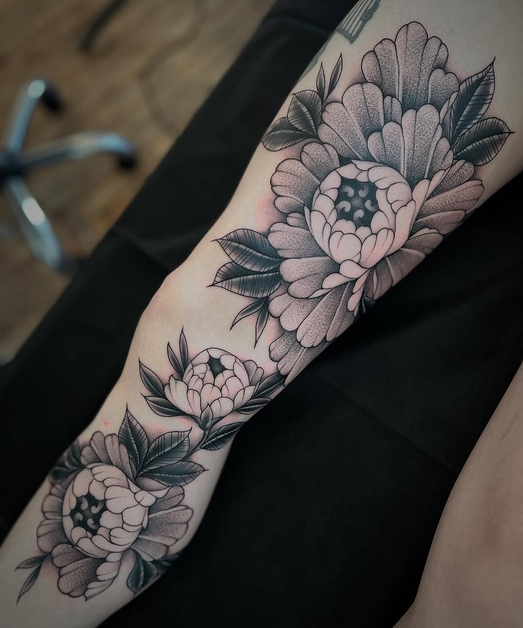Monochrome peony bouquet winds along forearm with stipple shading