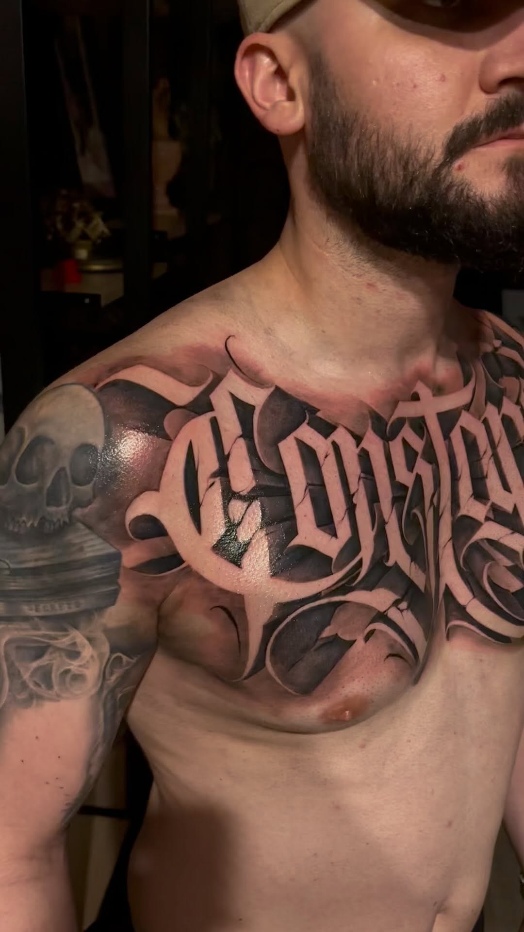 Bold blackletter script spanning chest with skull shoulder accent