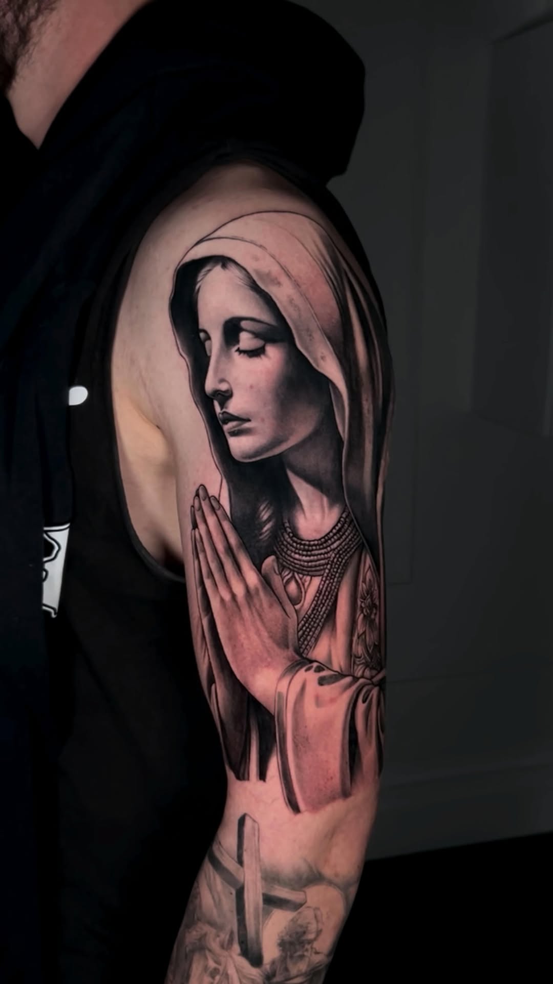 Somber grayscale Virgin Mary with praying hands, hooded