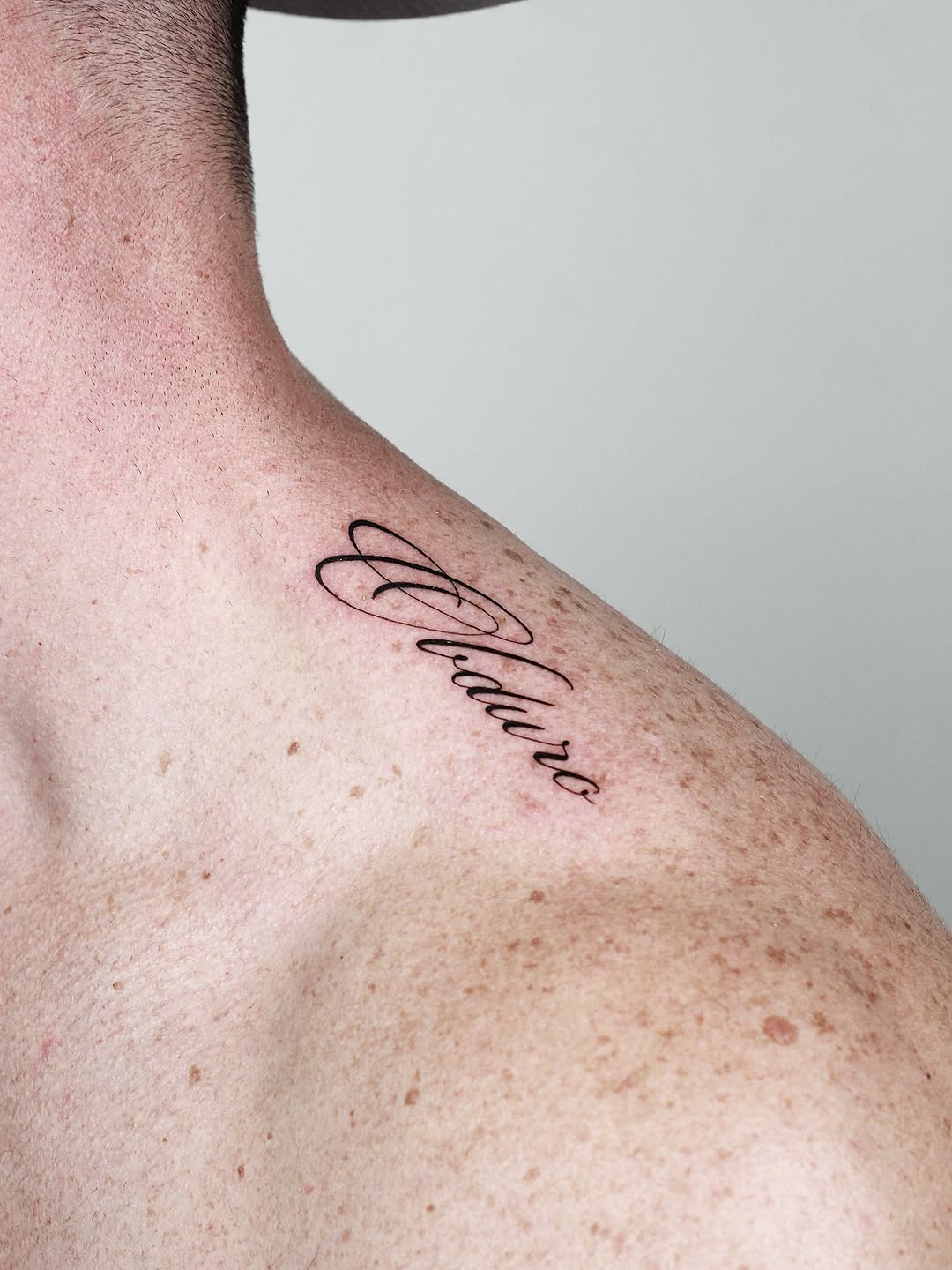 Elegant cursive word tattoo along the shoulder blade.