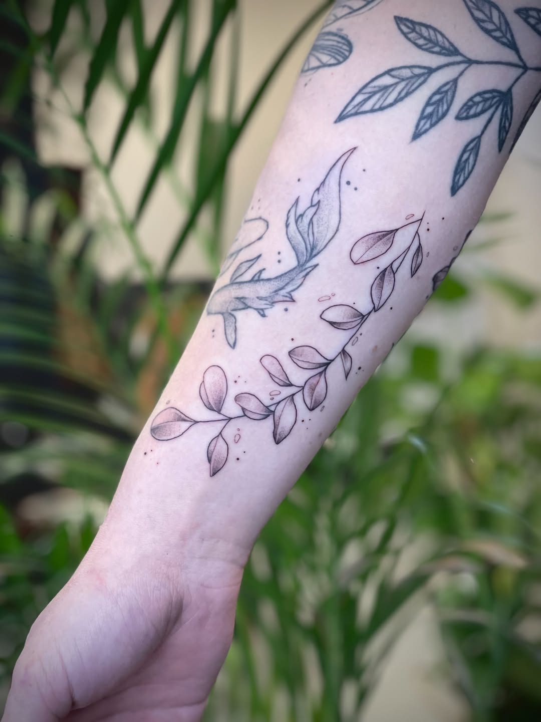 Delicate fine-line botanical leaves wrap the forearm.