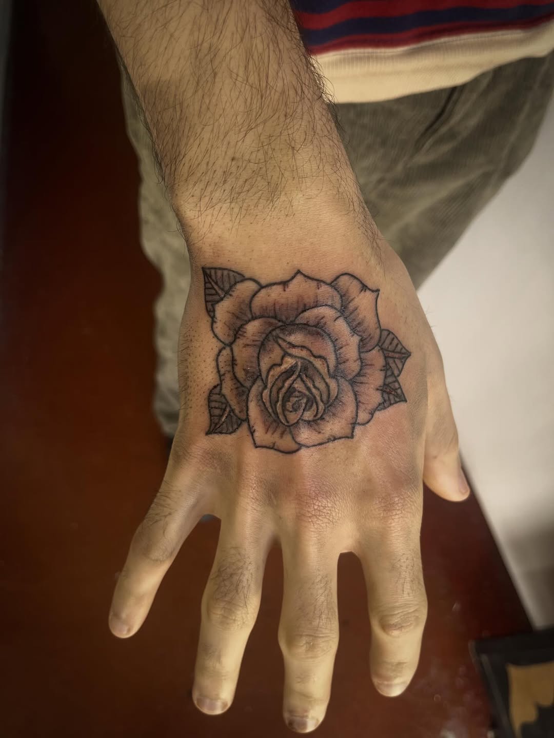 Bold traditional rose on the back of the hand, crisp linework.