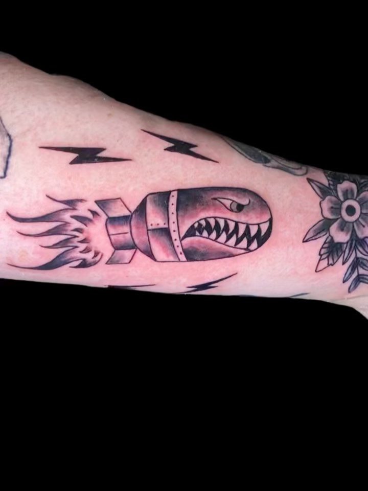 Bold illustrative rocket-torpedo with shark-teeth and flames on forearm.