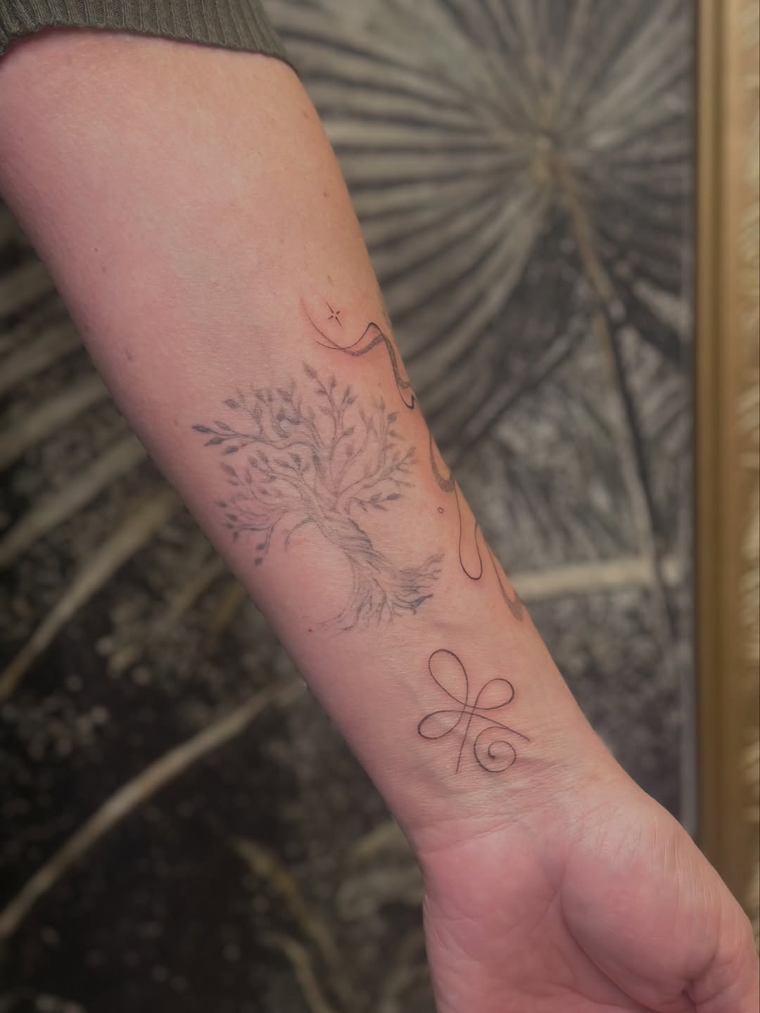 Delicate fineline tree with leaves and looping curve on forearm
