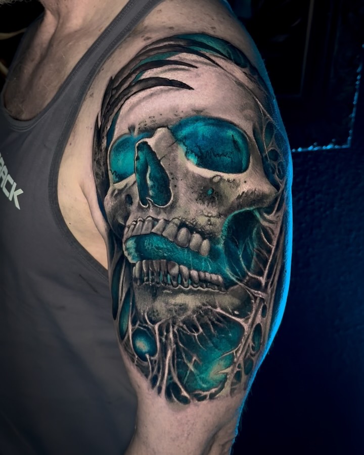 Teal-glow skull on shoulder with high-contrast blackwork.