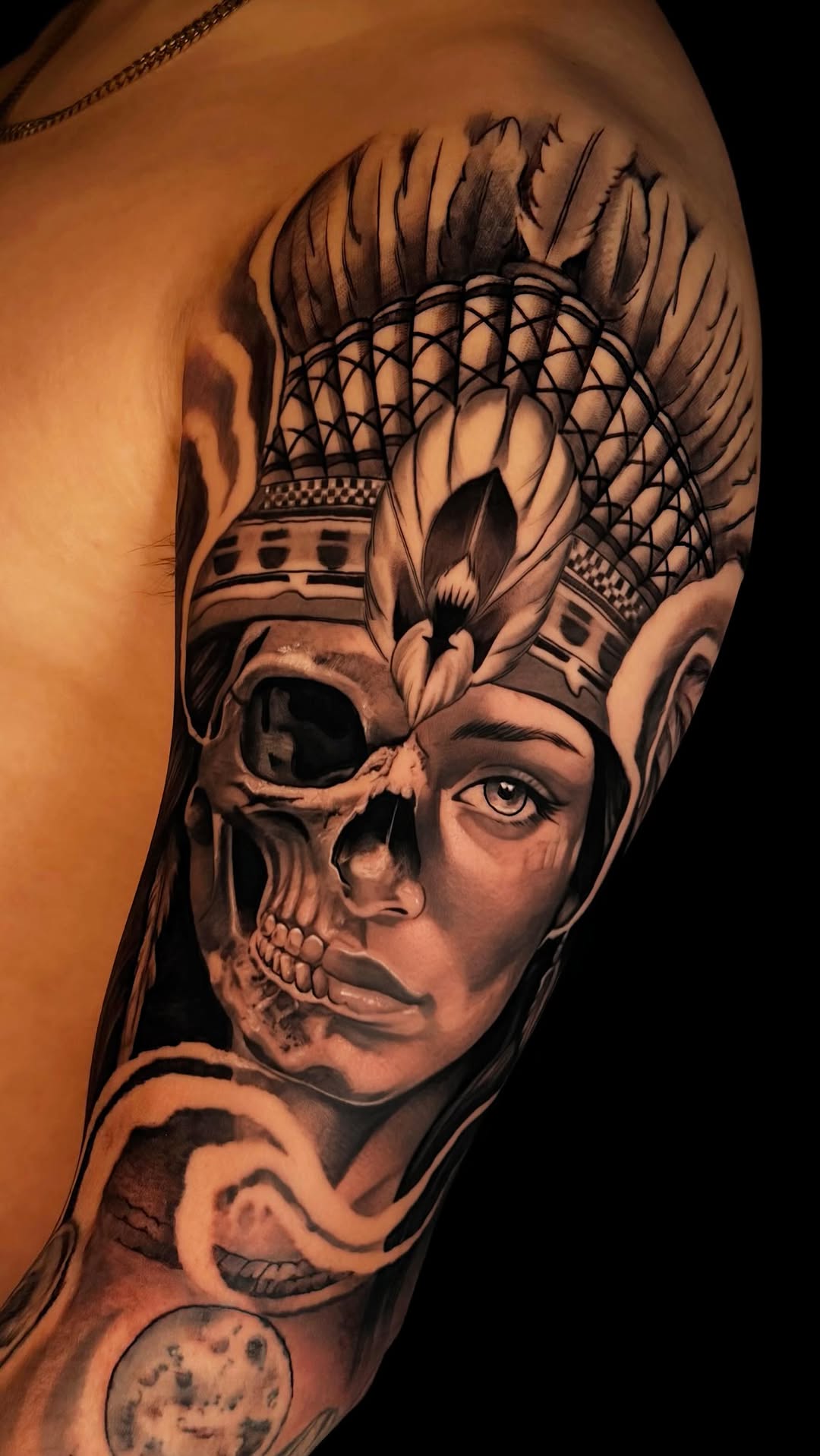 Dramatic black-and-gray realism of skull-faced figure with feathered headdress