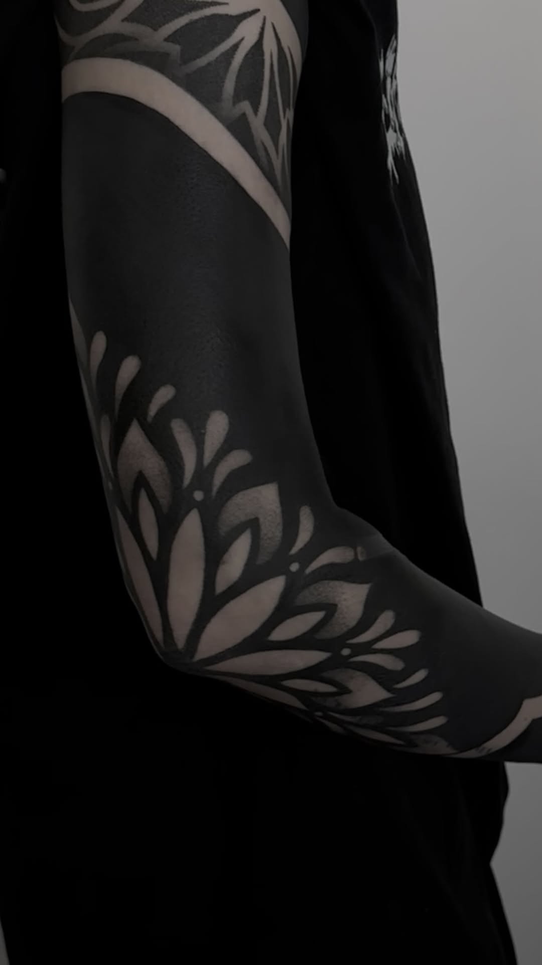 Bold blackwork botanical forearm sleeve with negative-space leaves