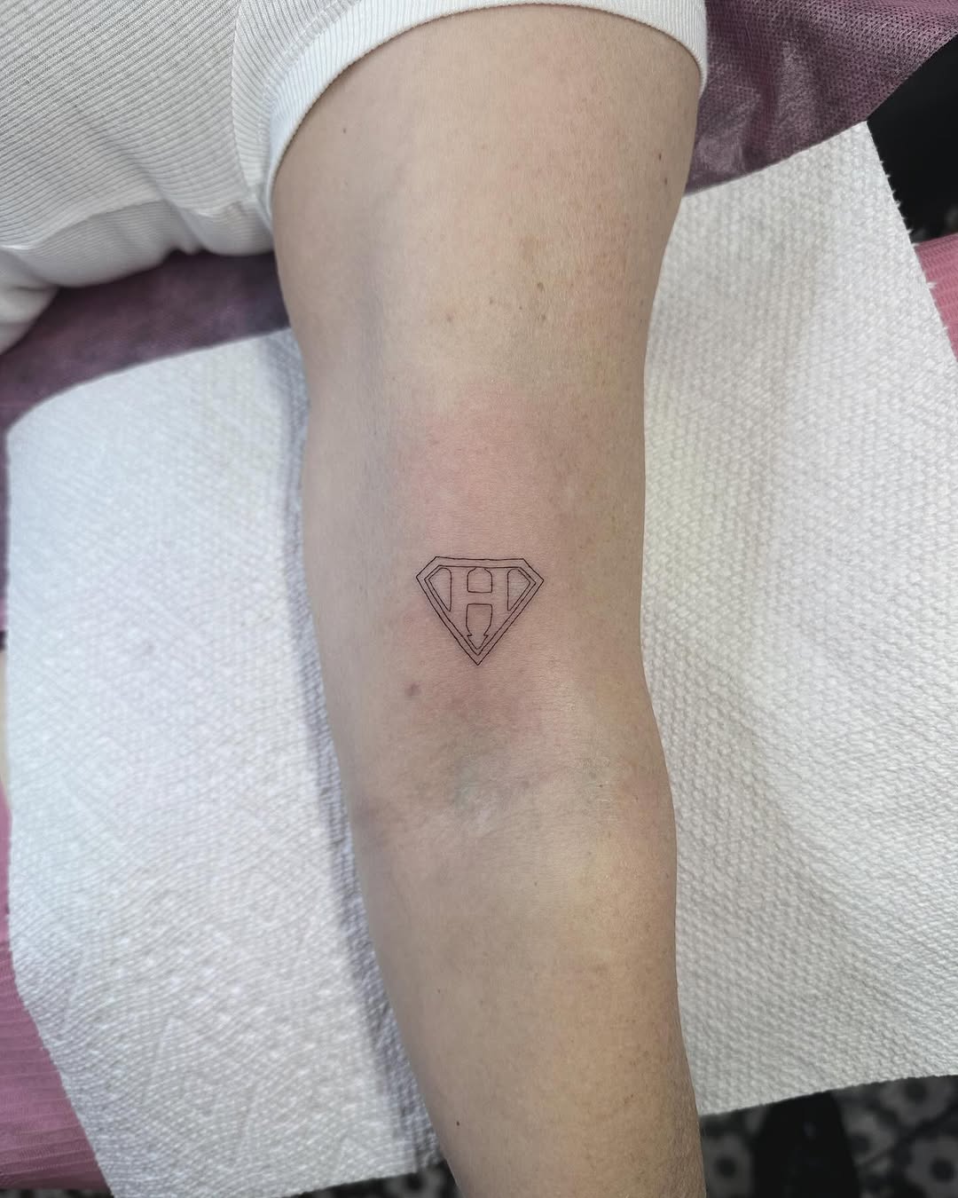 Tiny minimalist diamond shield with letter H, fine-line.