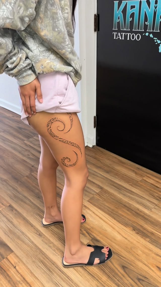 Bold black tribal spiral band with ornamental motifs on outer thigh