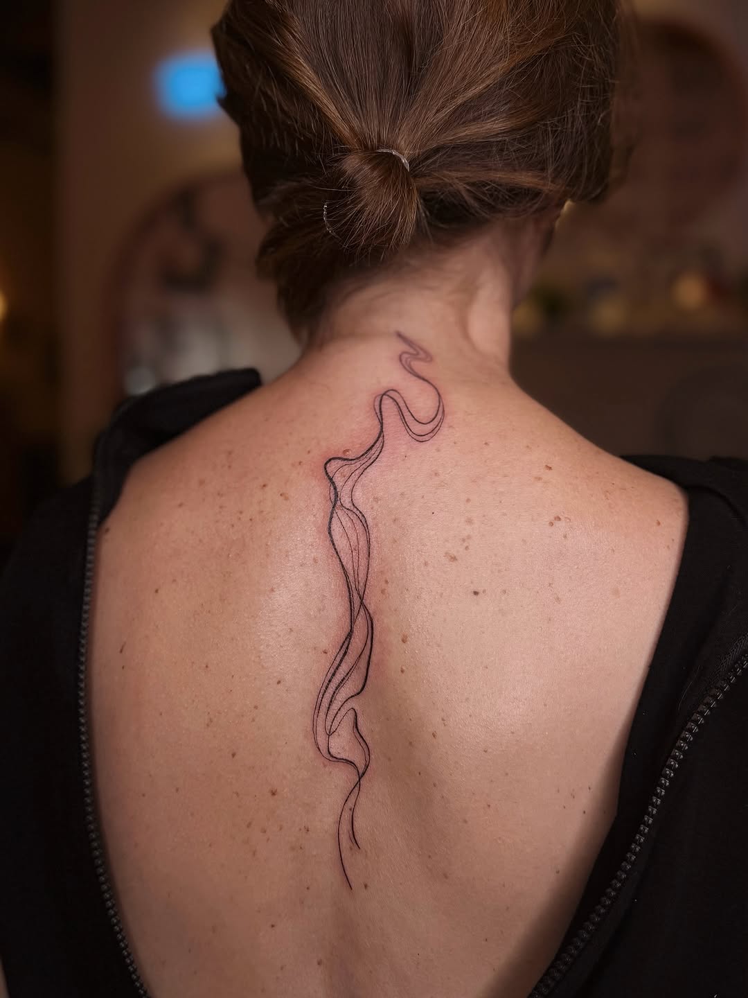 Delicate, flowing black-line spine tattoo with wispy contours.