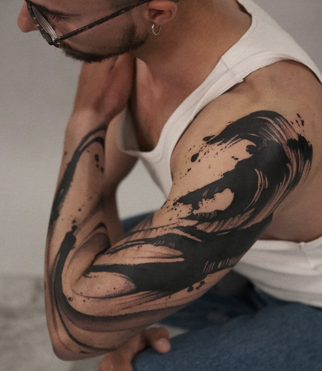 Bold black brush-stroke abstract tattoo on upper arm