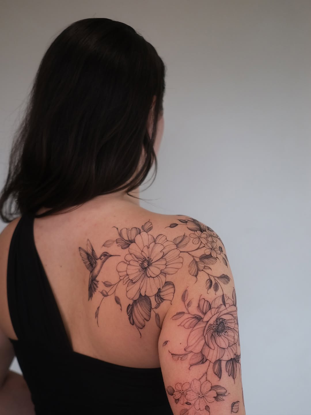 Intricate floral shoulder piece with hummingbird, fine-line botanicals.