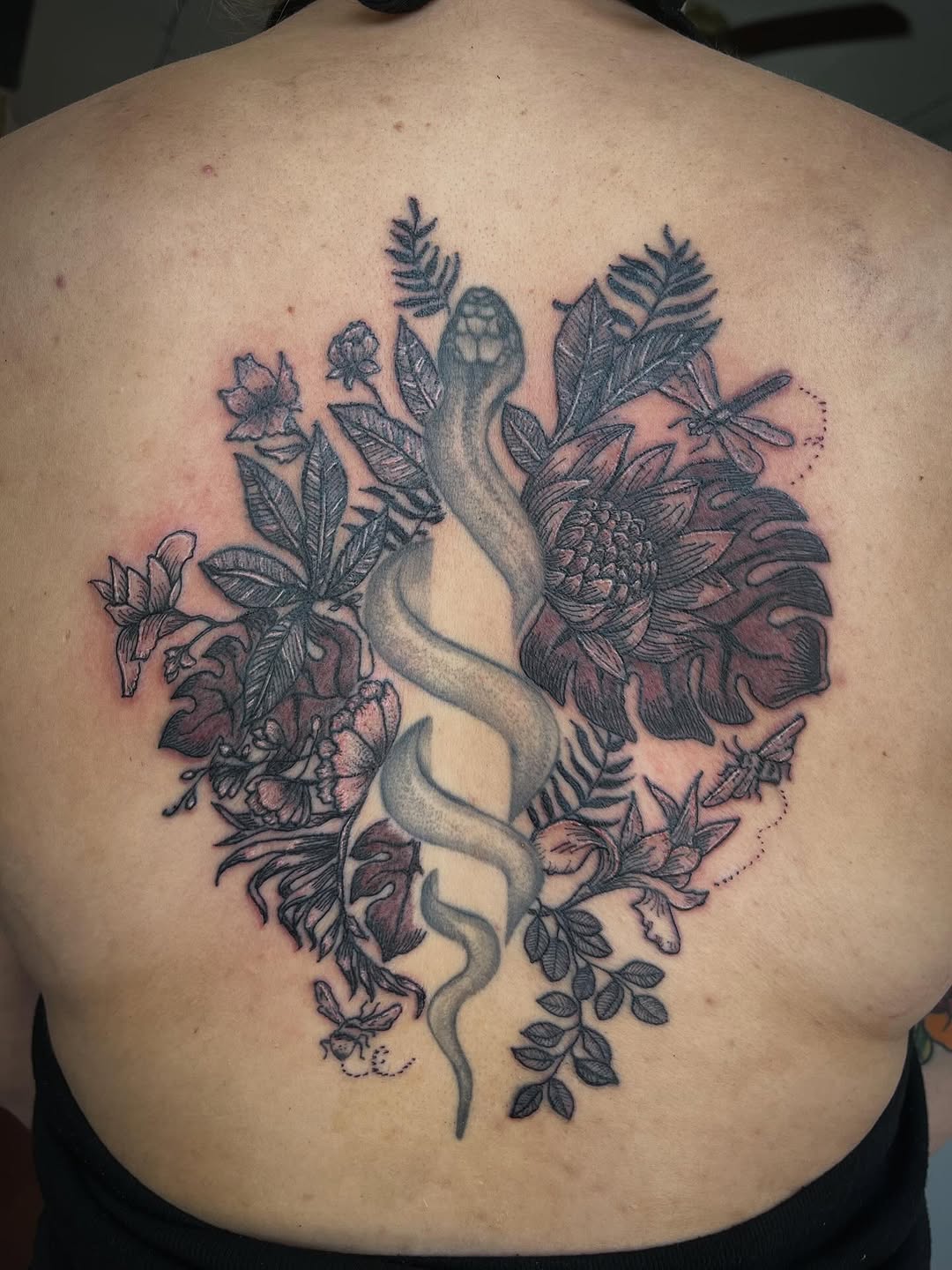 Intricate back piece with twisting serpent amid lush florals.