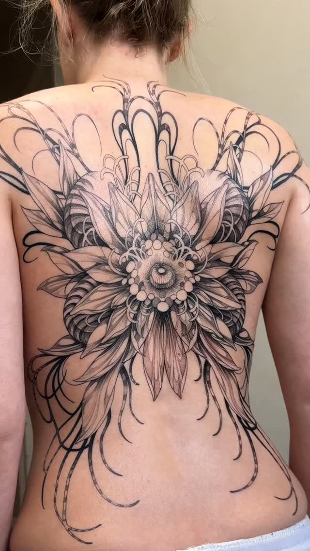 Intricate blackwork back piece with a radiating dahlia-like bloom