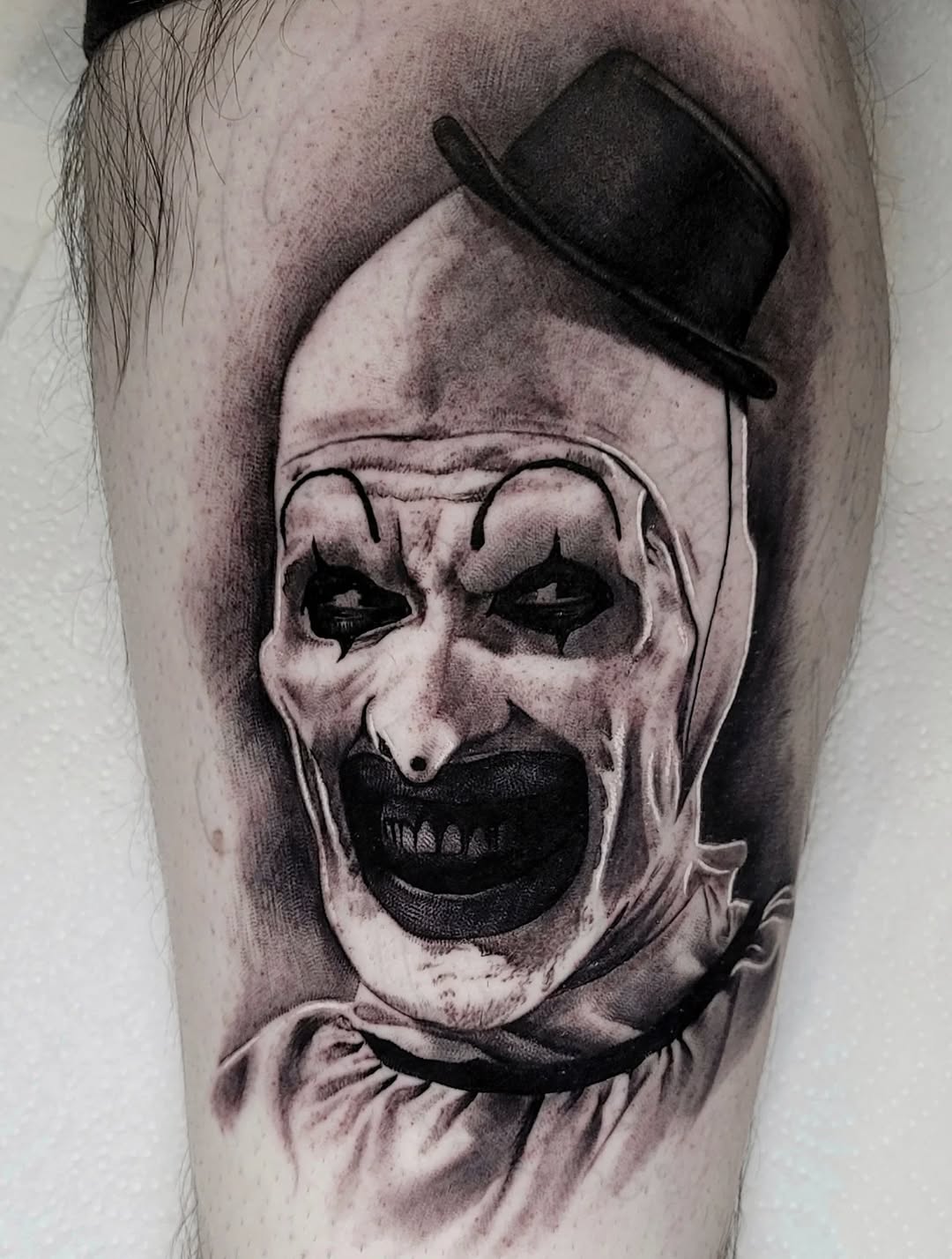 Hyper-detailed black-and-gray horror clown portrait on upper arm.