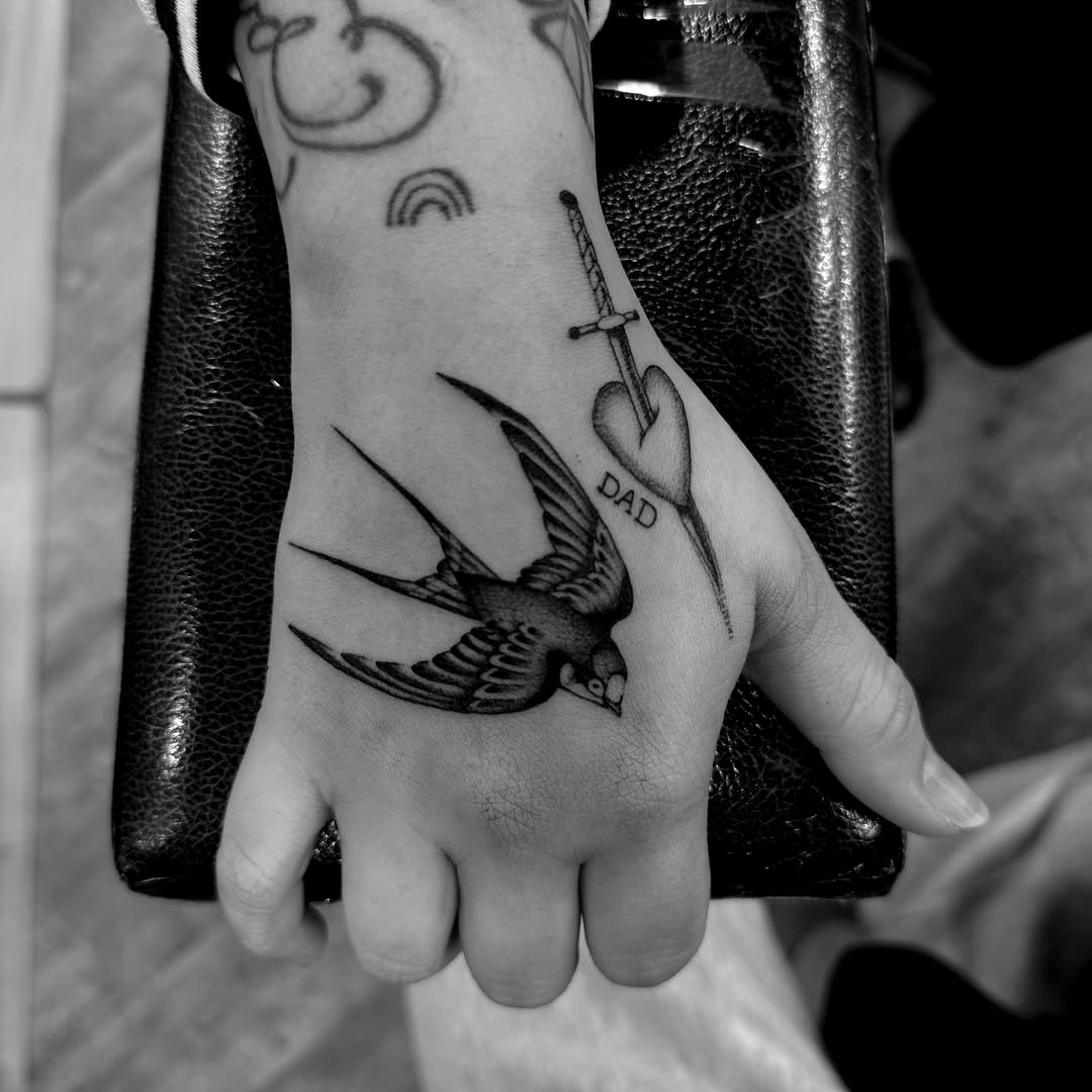 Bold swallow and heart-dagger memorial tattoo on hand