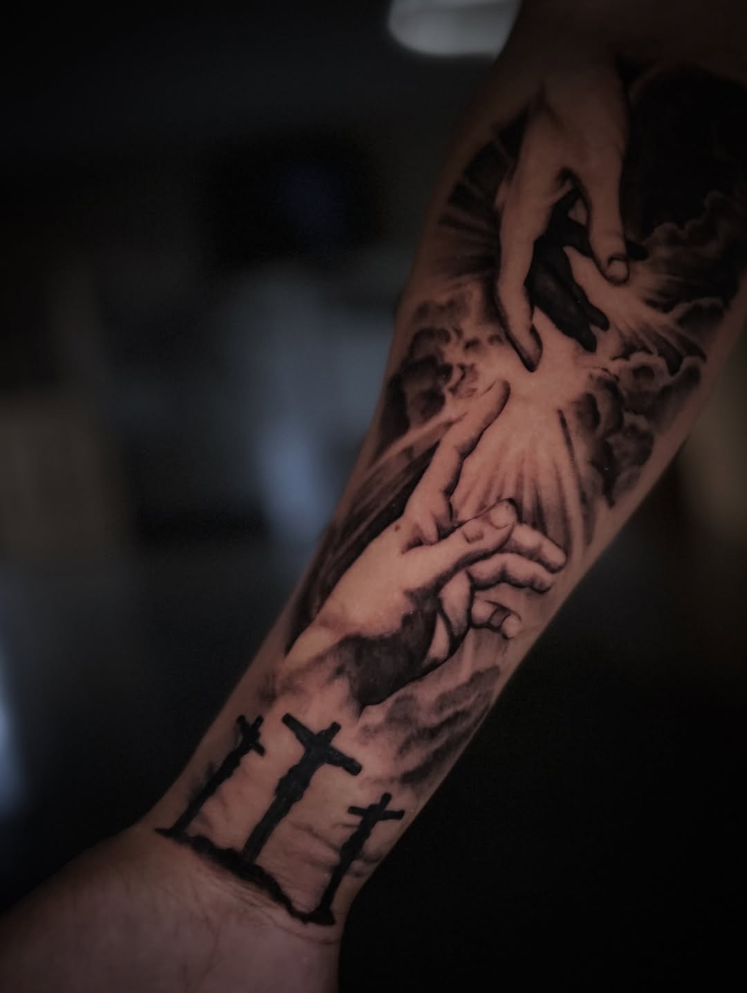 Dramatic grayscale prayer-hands with three crosses on forearm