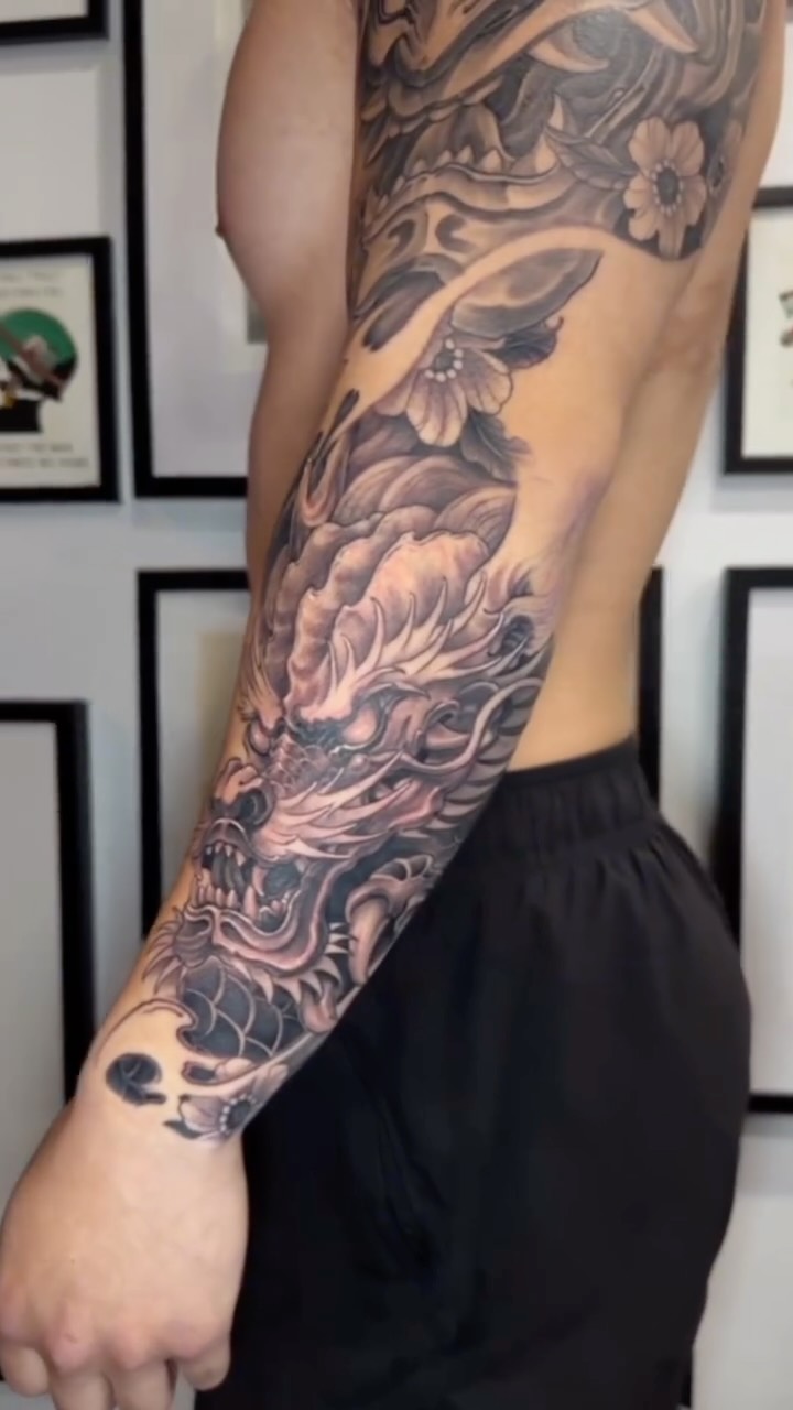 Bold oriental dragon coils through a shadowed black-gray forearm sleeve