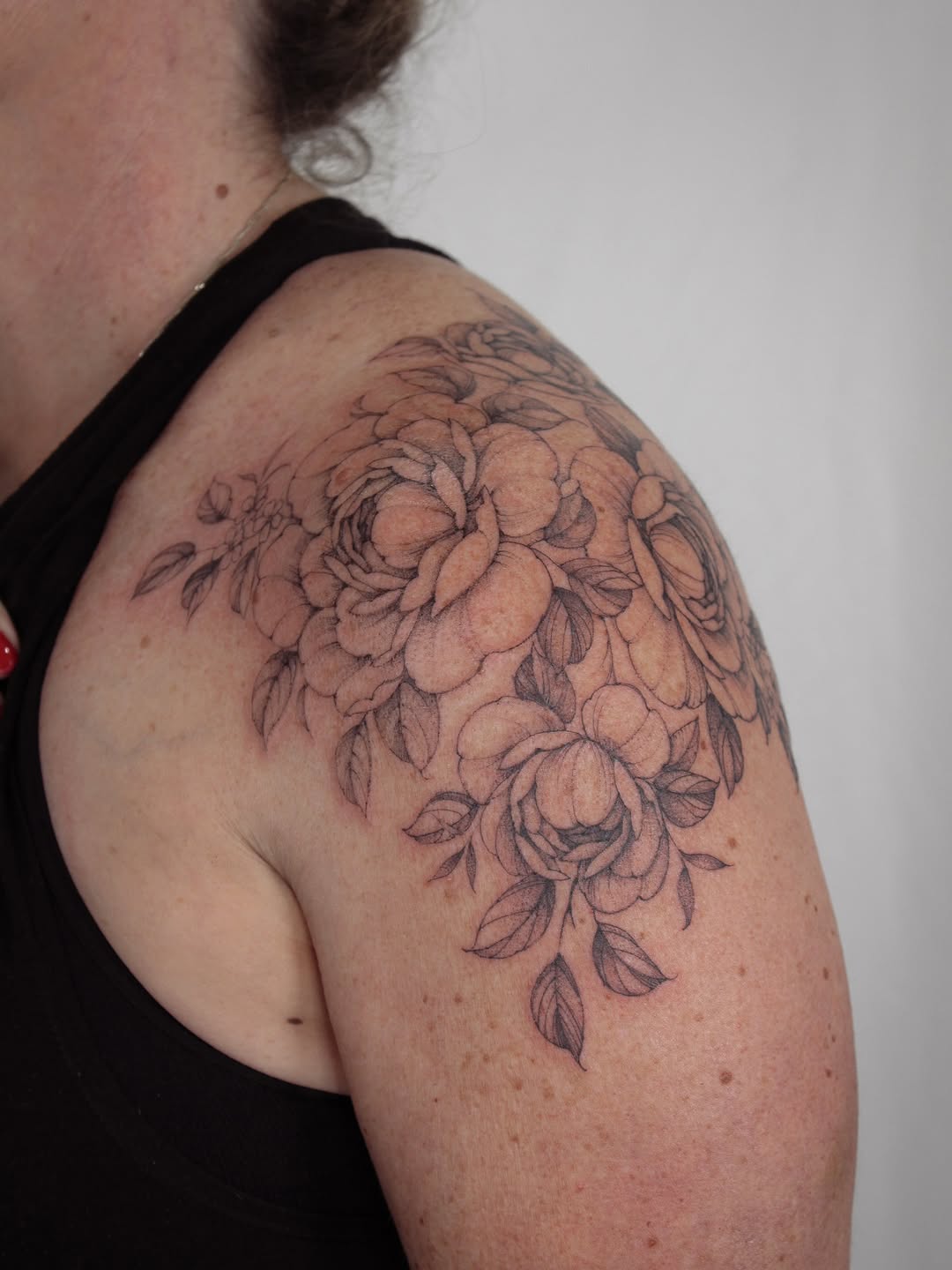 Intricate peony bouquet wraps shoulder in delicate fine-line work.