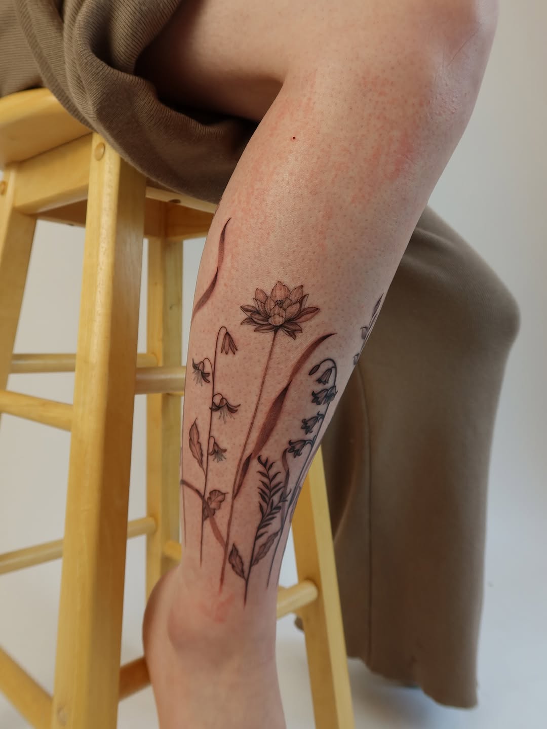 Delicate fine-line botanical leg tattoo featuring a lotus bloom
