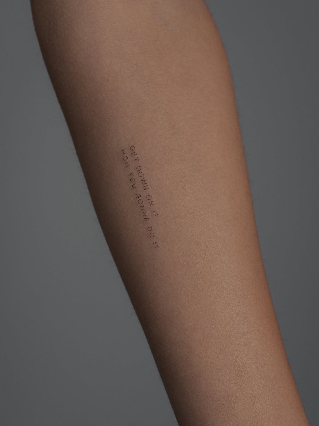 Tiny uppercase quote in micro lettering along forearm.