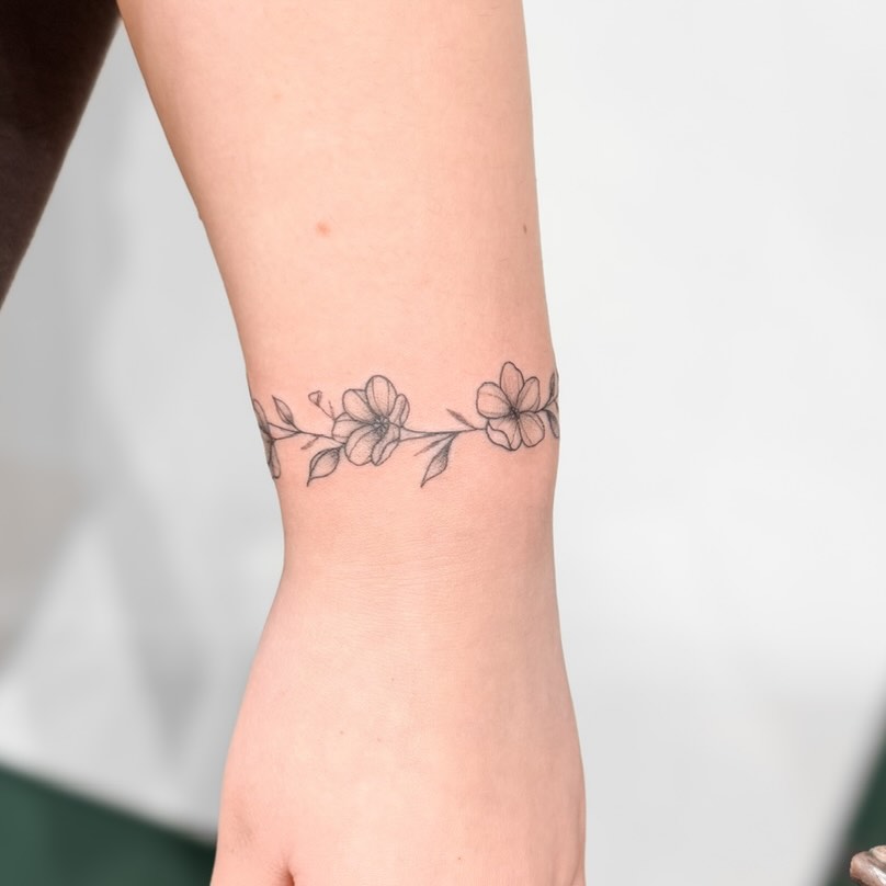 Delicate fine-line floral band around inner forearm.