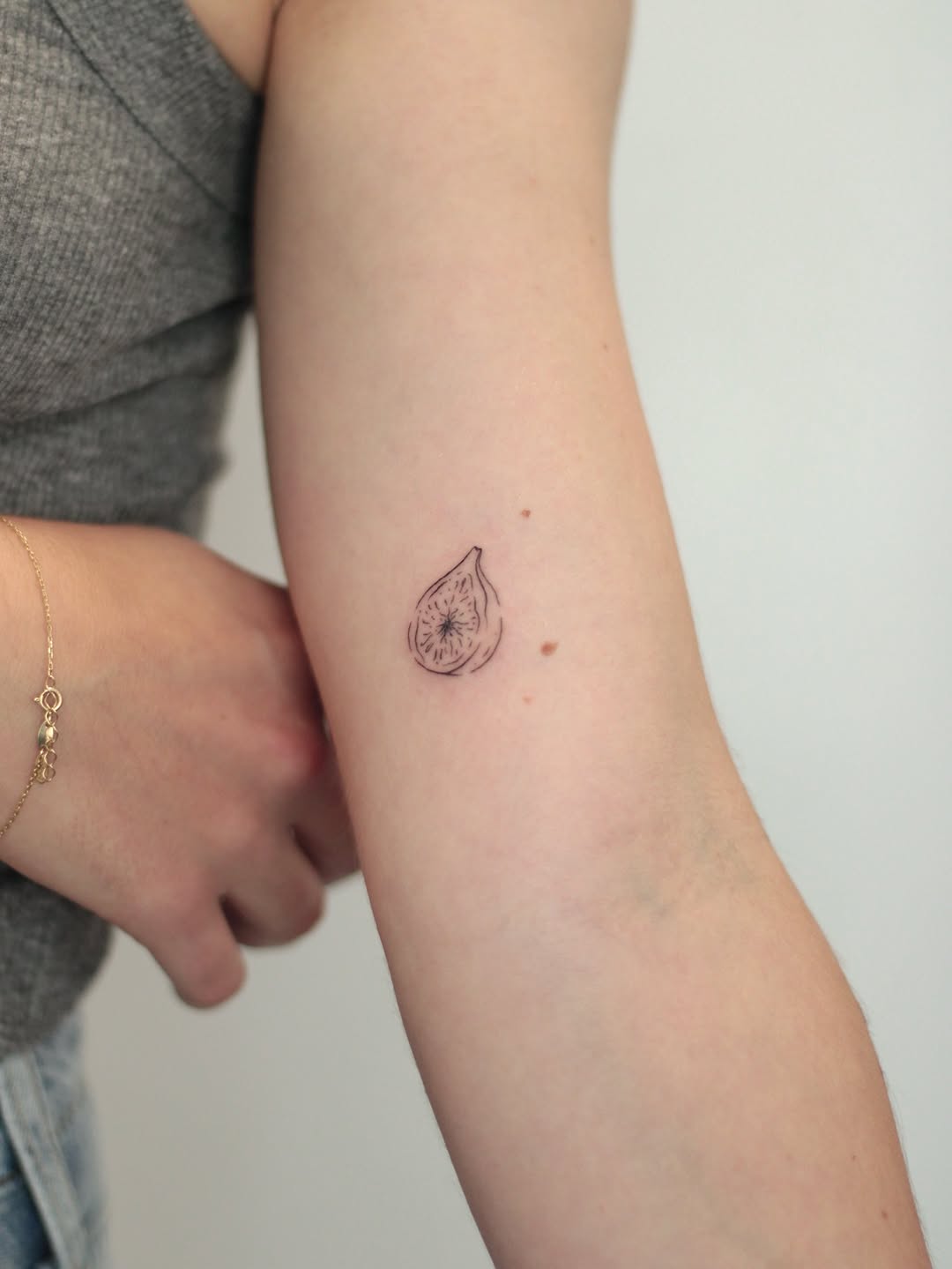 Delicate fine-line fig fruit tattoo on forearm