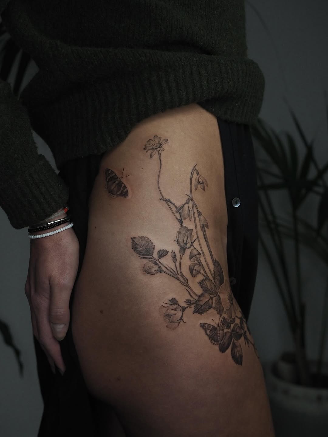 Delicate black-and-gray botanical thigh piece with daisies and butterflies.