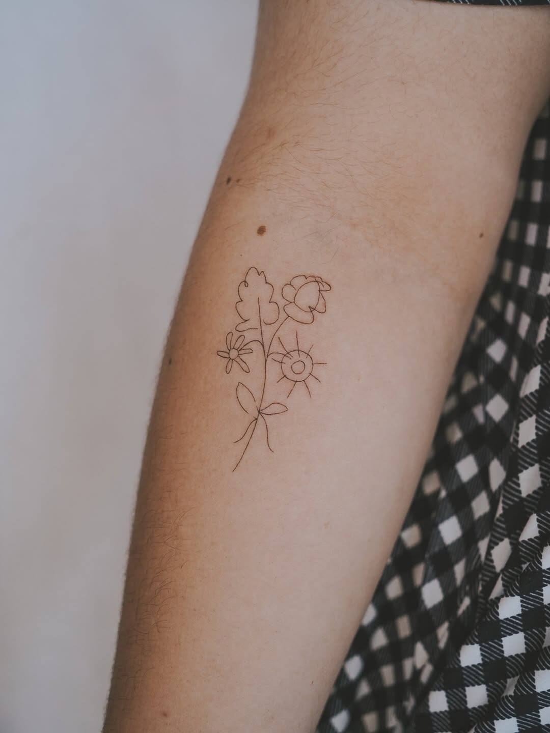 Delicate fineline floral trio with sun accent on forearm
