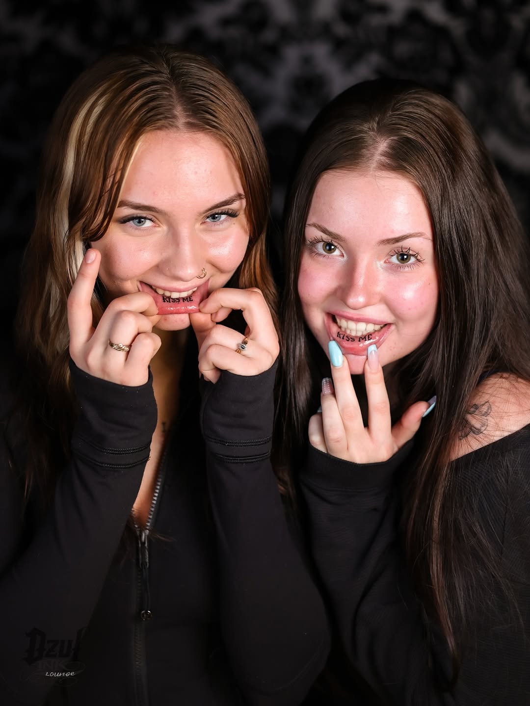 Two women showcase lip tattoos with bold 'KISS ME'.