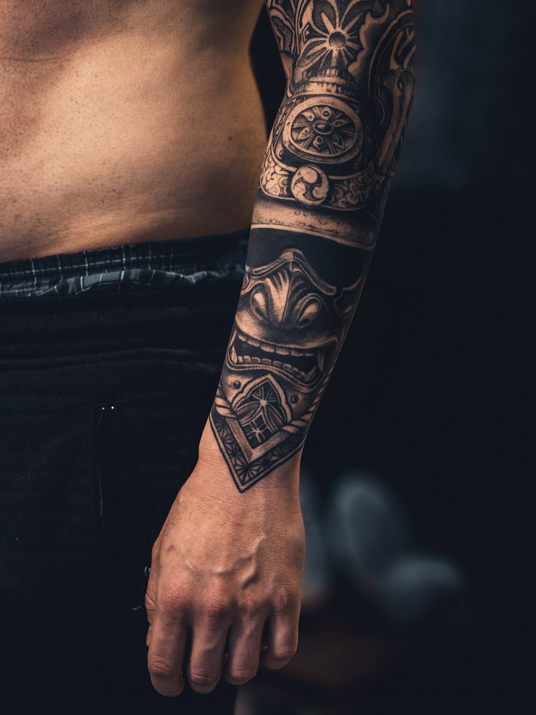 Intricate black-and-gray forearm sleeve with demon mask and ornamental wheel