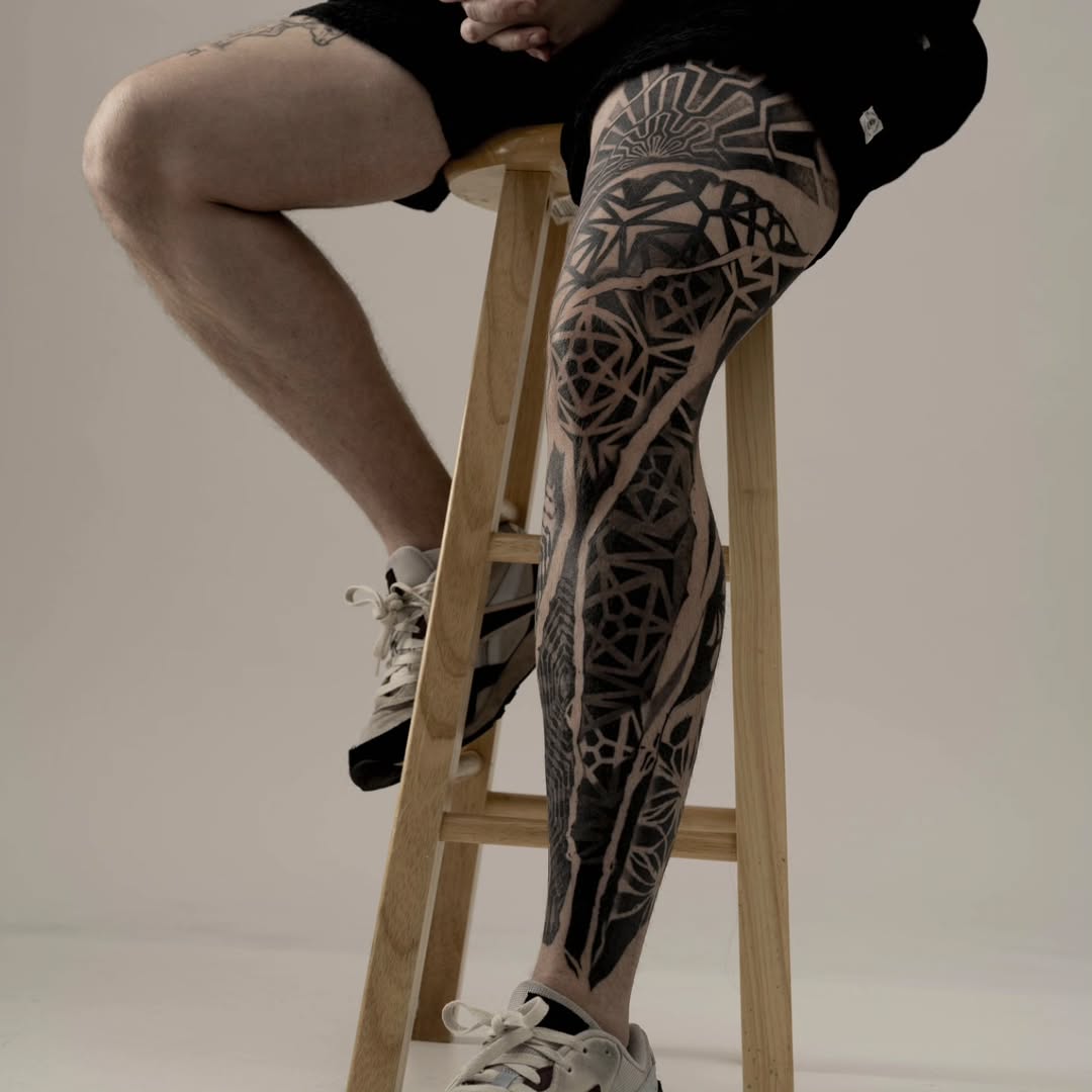 Bold geometric blackwork leg sleeve with intricate negative-space patterns