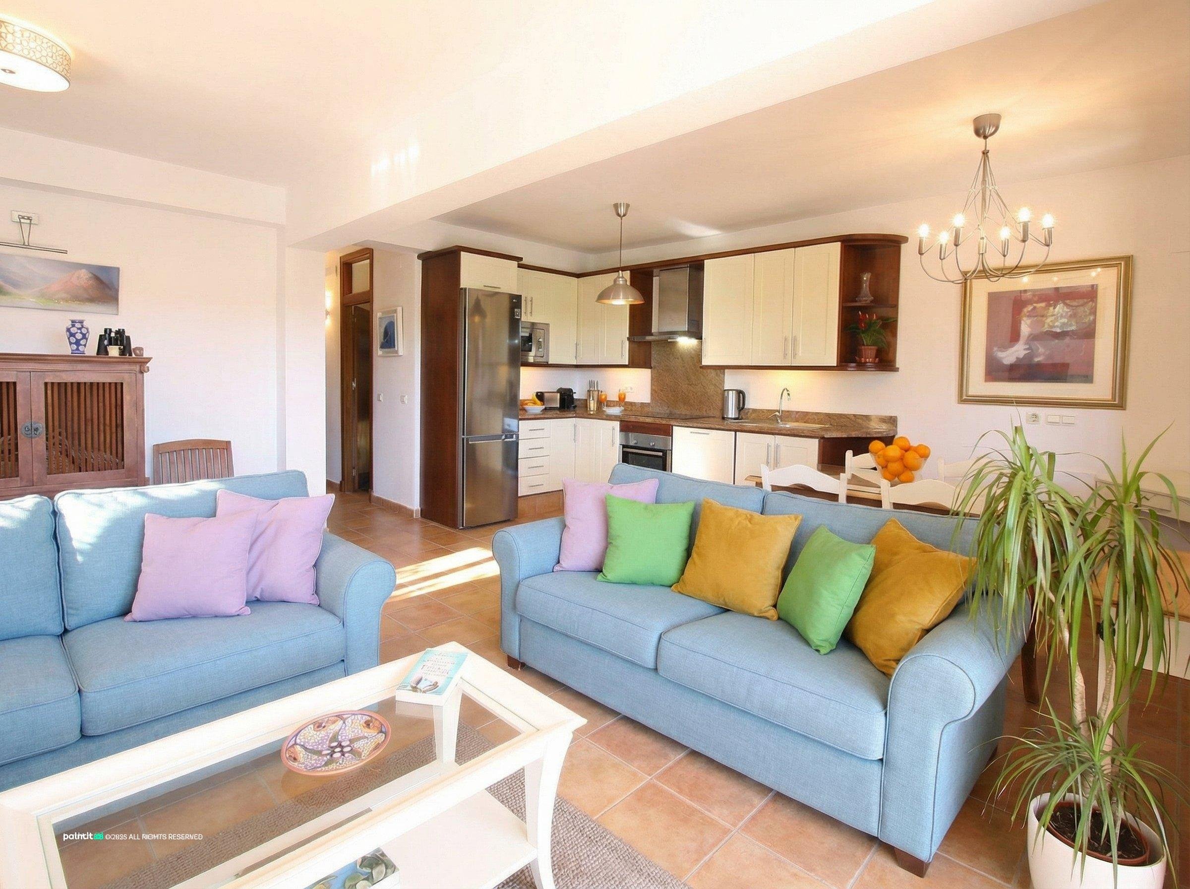 Living room with two light blue sofas, yellow and pink cushions and an open kitchen behind