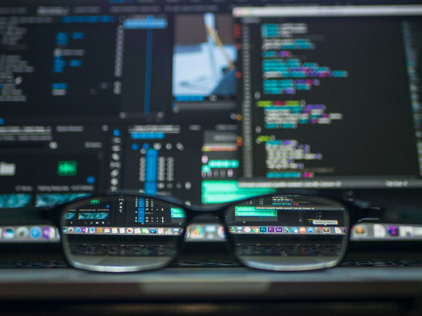 A pair of eyeglasses on a keyboard bringing blurred code and editing windows into sharp focus