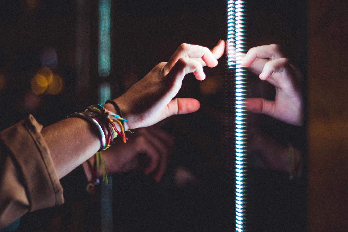 Hands reaching toward a narrow strip of bright light on a dark reflective surface