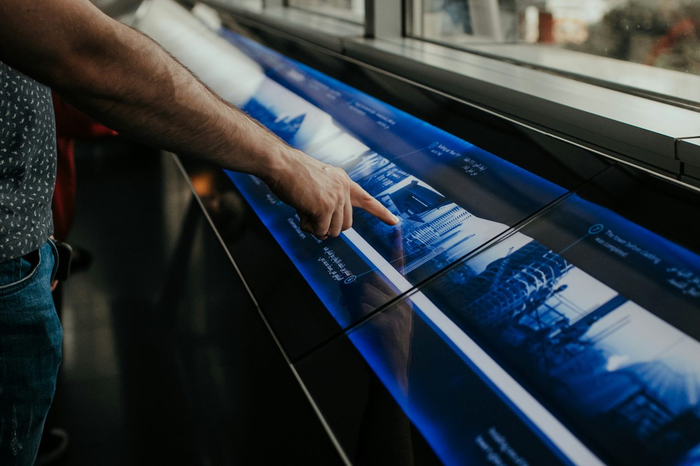 A man pressing a point on a large illuminated blue touchscreen information panel