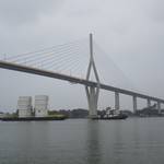 Two large white fiberglass reinforced plastic (FRP) tanks on a barge being transported under a cable-stayed bridge.