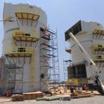 Two large white FRP tanks with yellow gratings and stairs installed at a construction site, featuring scaffolding and crane equipment.