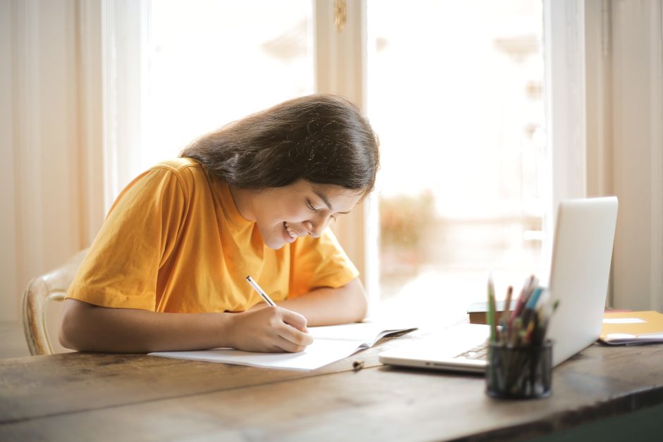 Young woman studying with a laptop and notepad at home, smiling