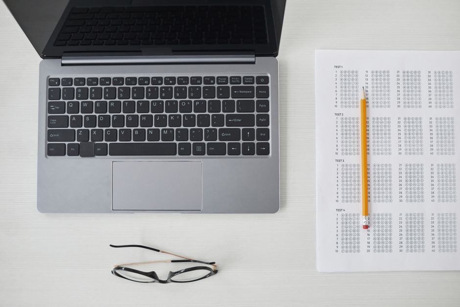 Flat lay of a laptop, exam sheet, and pencil on a white desk