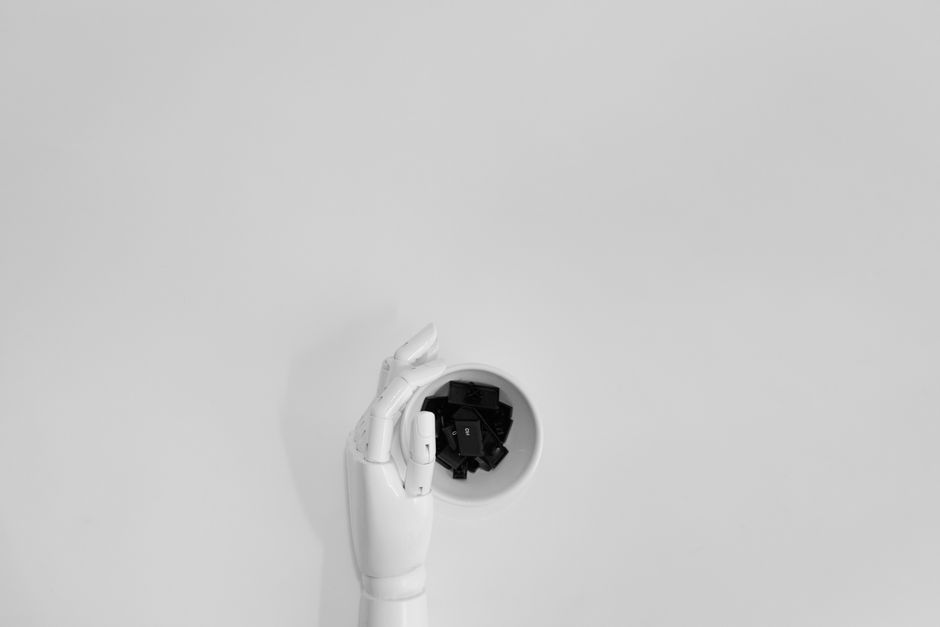 A robotic hand grasping black keyboard keys in a minimalist setting