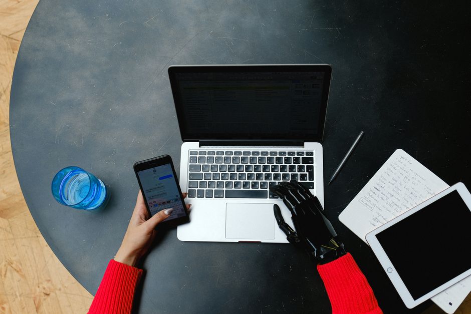 A person using a laptop, smartphone, and tablet with a prosthetic hand