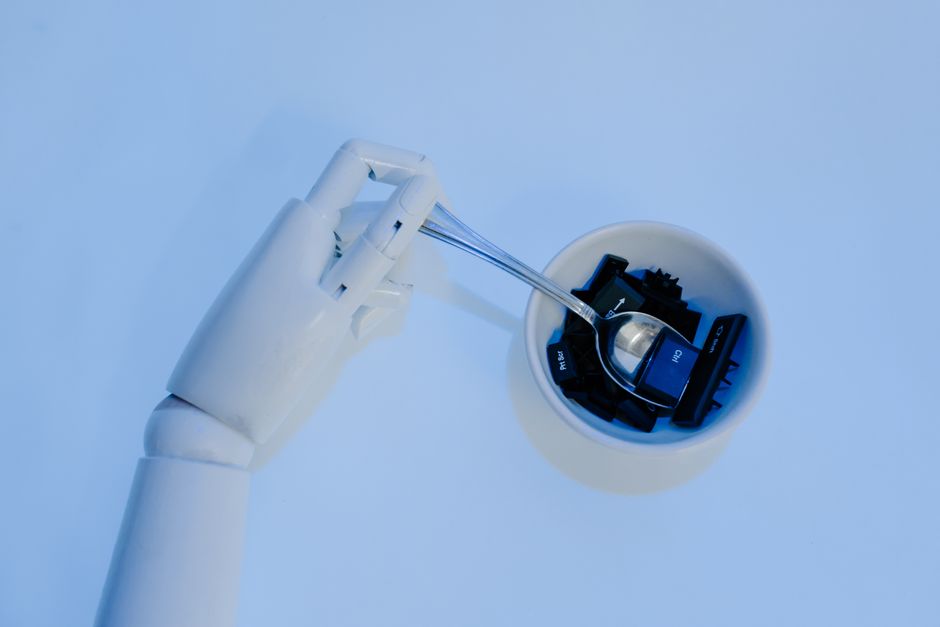 A robotic hand holds a spoon filled with keyboard keys, symbolizing precision