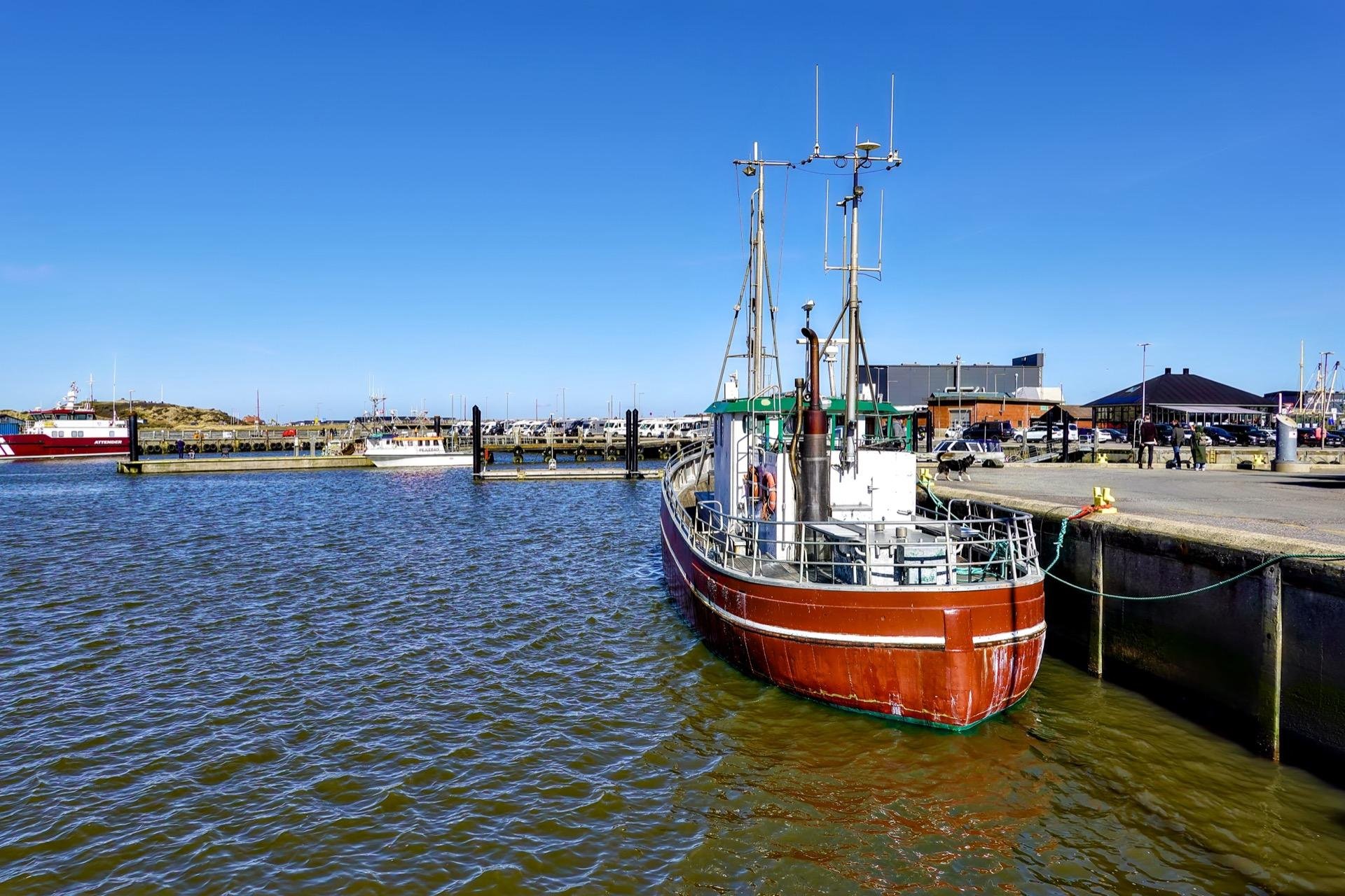 A boat in the harbour, red and white colored before a blue sky in an absolutely calm environment.