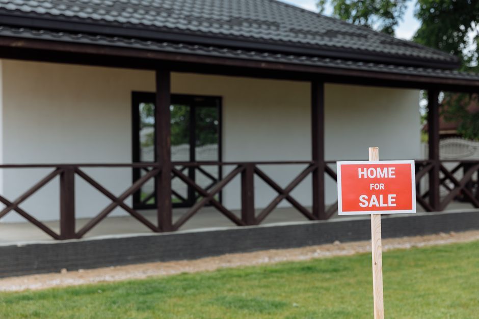 A suburban house exterior with a for sale sign in the front yard