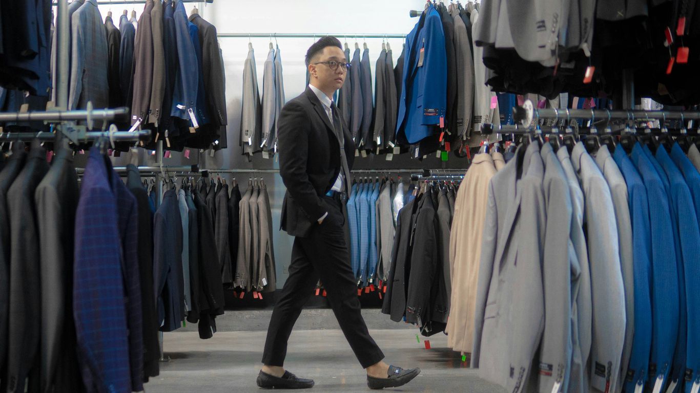 man in gray suit standing near clothes hanged on rack