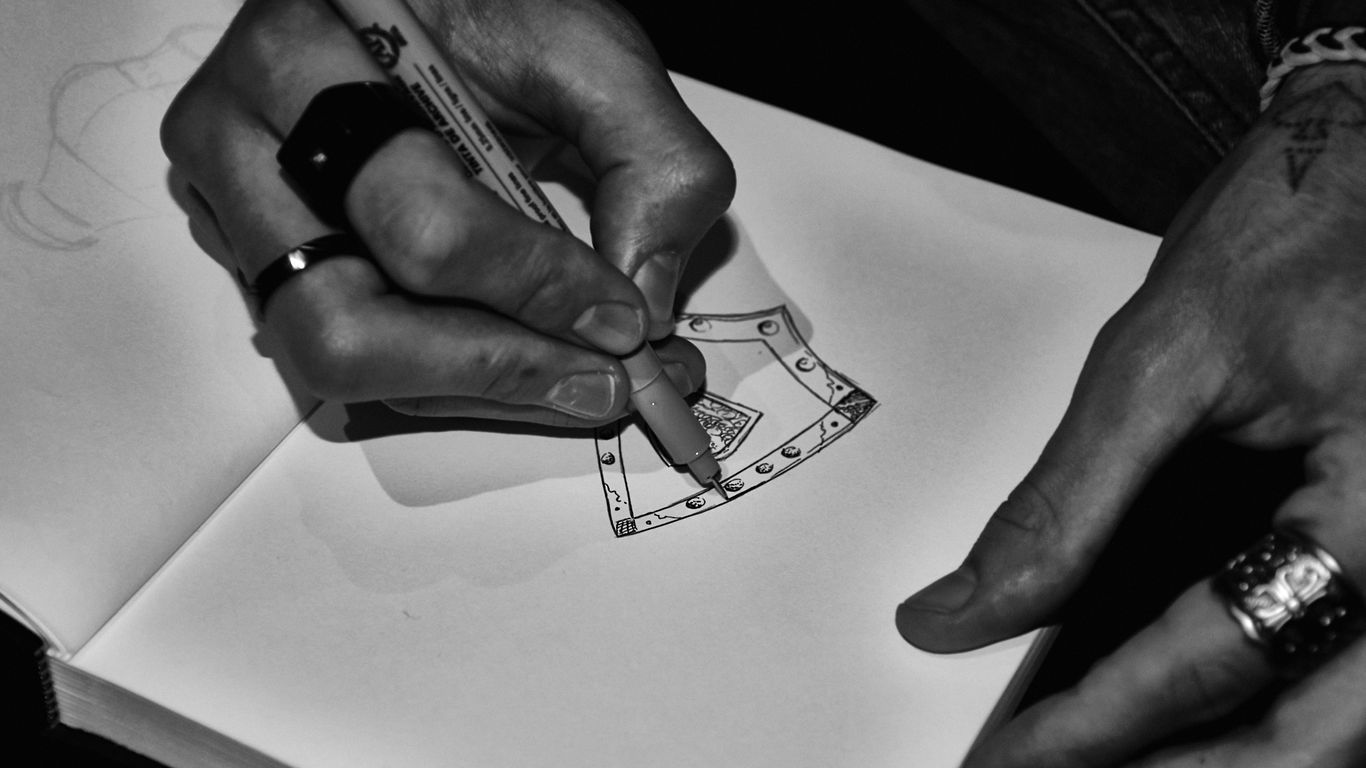 Hands drawing an axe design in a sketchbook