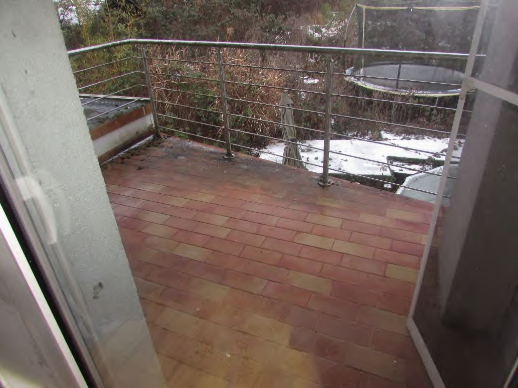 Terrasse mit roten Pflastersteinen und Metallgeländer, im Hintergrund Schnee und Vegetation