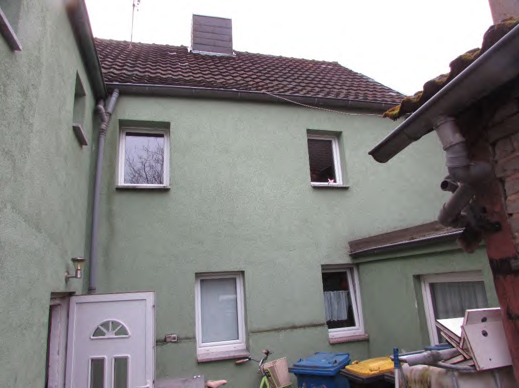 Rückansicht eines Einfamilienhauses mit grüner Fassade, Ziegeldach, Fenstern und einer Tür im Hofbereich