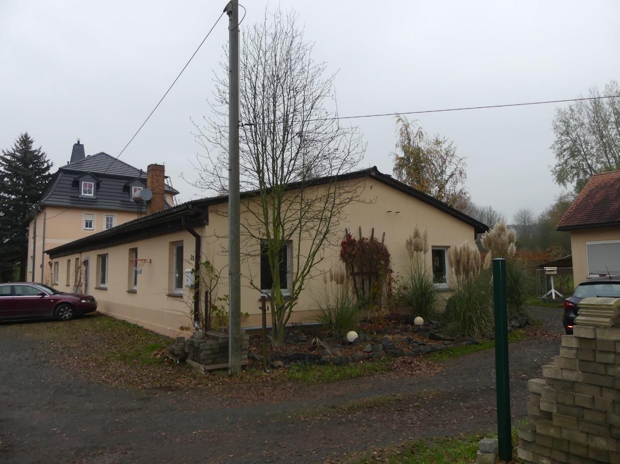 Seitenansicht eines beigefarbenen Wohnhauses mit Gartenanlage, Bäumen und gepflastertem Vorplatz, Döbelner Straße 25, Nossen